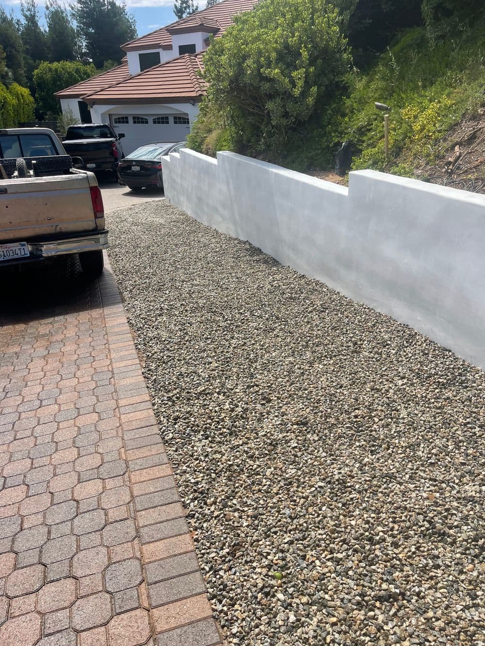 Gravel driveway beside a white wall and parked cars in a residential area.