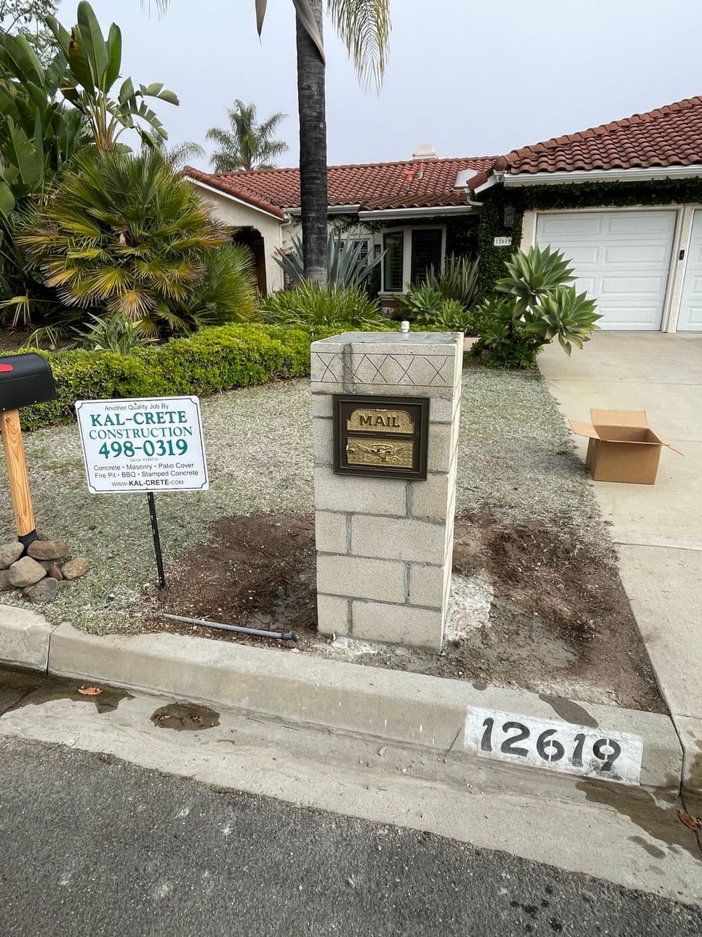 Mailbox in front of a house with a construction sign and tropical plants, in a residential area.