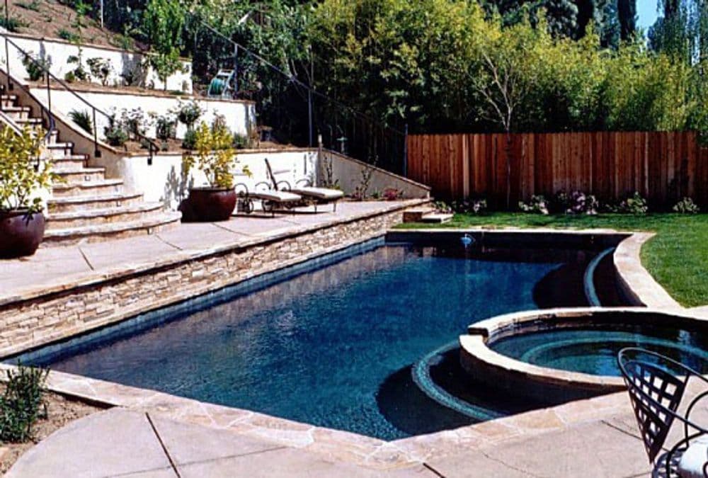 Backyard oasis featuring a swimming pool, spa, stone steps, and landscaped greenery.