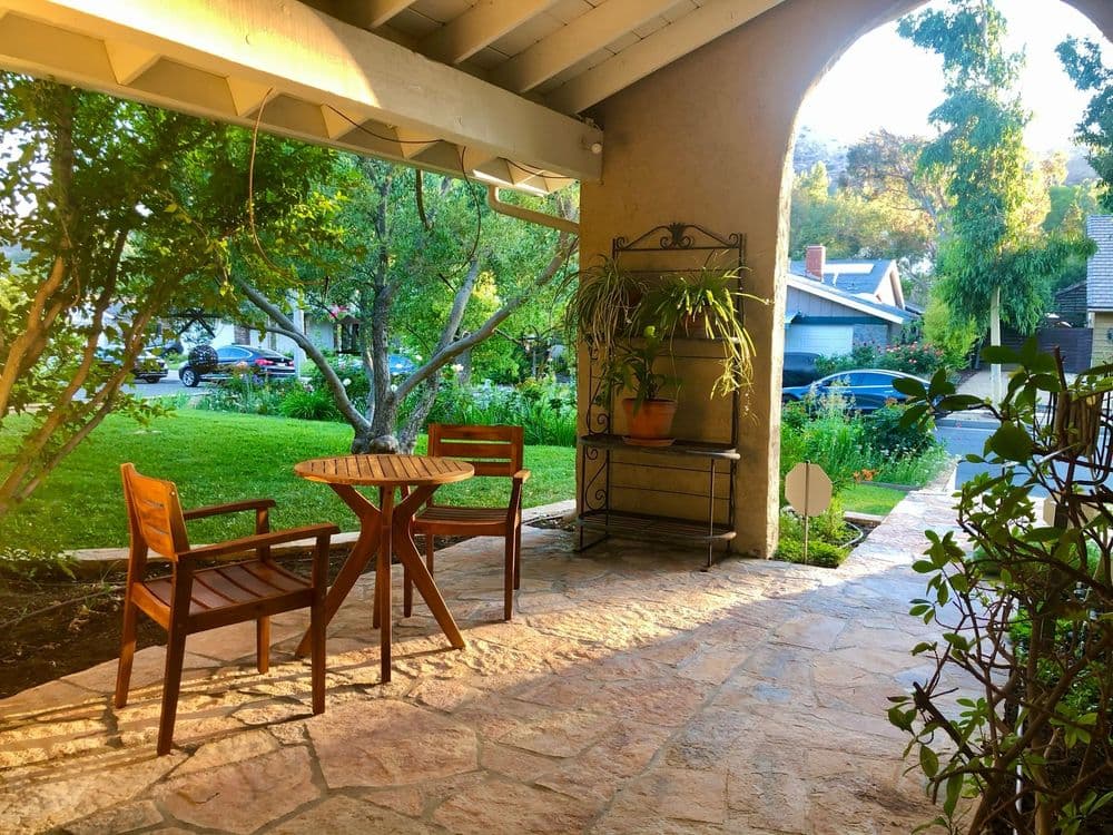 Cozy porch with wooden chairs, a table, and lush greenery in a charming neighborhood.