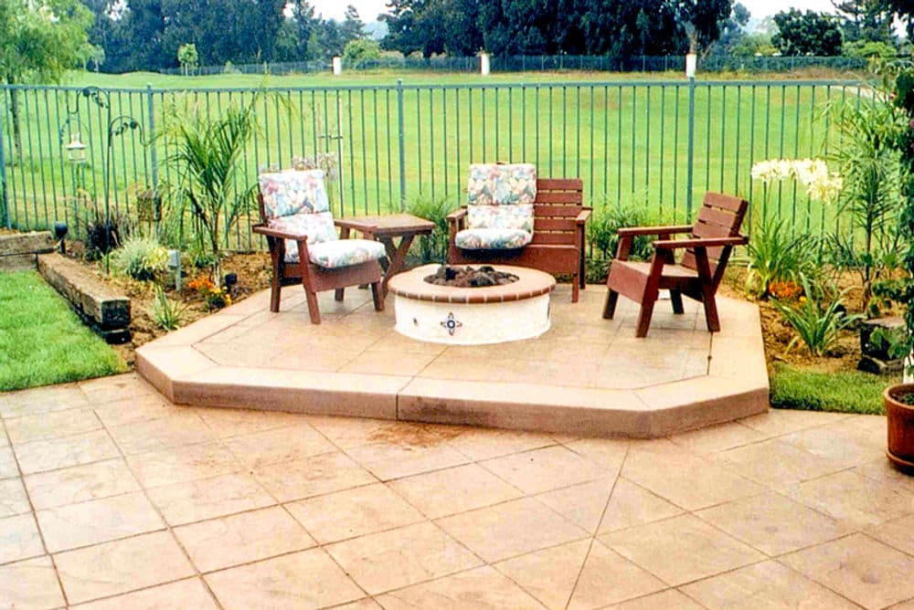 Outdoor patio with two wooden chairs around a fire pit, surrounded by garden plants.